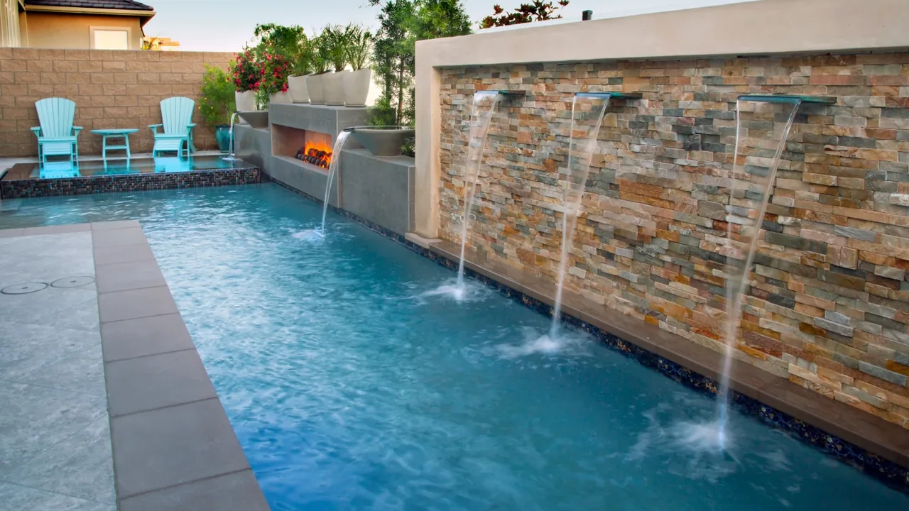 Elegant pool and spa combination remodel with stone tile accents and water features